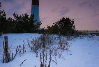 A portrait orientation HDR photograph of the Barnegat Lighthouse at sunset in snow.