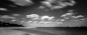 An afternoon long exposure photograph taken from High Bar Harbor in Barnegat Light overlooking east toward the Barnegat Lighthouse. In this empty bay beach scene, the low level clouds streak across this black and white photograph from left to right.