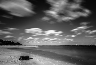 An afternoon long exposure photograph taken from High Bar Harbor in Barnegat Light overlooking east toward the Barnegat Lighthouse. In this empty bay beach scene, the low level clouds streak across this black and white photograph from left to right.