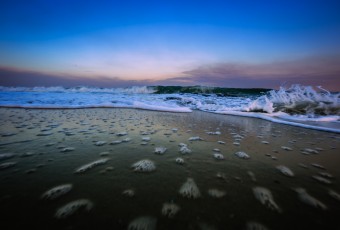 A ground level perspective wide angle photograph of an ocean break during blue hour in Ship Bottom, NJ, on Long Beach Island. Foreground bubbles are left behind the retreating waves.