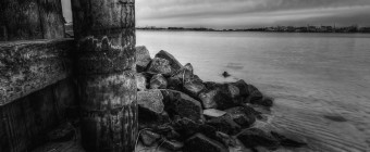 A seven frame black and white composite exposure of a wooden bulkhead and mounded jetty rock define the portrait orientation scene with Barnegat Bay expanding off to the right.