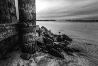A seven frame black and white composite exposure of a wooden bulkhead and mounded jetty rock define the portrait orientation scene with Barnegat Bay expanding off to the right.
