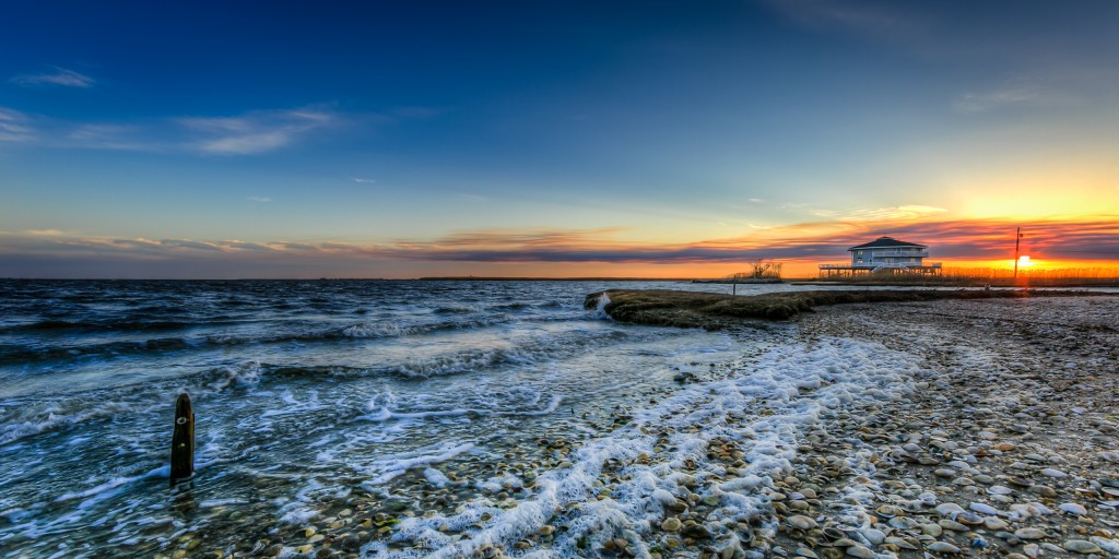 An HDR photograph taken at sunset from the east end of Cedar Run Dock Road. Rolling waves from Barnegat Bay move onshore leaving heavy foam upon the small shell-laden beachfront.