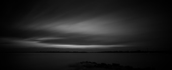 A low key long exposure black and white photograph taken over Barnegat Bay from Sunset Point in Ship Bottom, New Jersey. This photograph is marked by dark tones and strong contrast across the horizon.