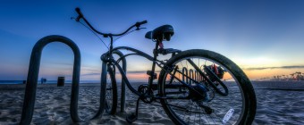An HDR photograph taken just after sunset during blue hour along the shores of Huntington Beach California. The foreground is marked by a sweet beach cruiser bicycle locked to a beach bound bike rack. The Pacific Coast Highway lies away in the distance.