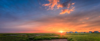 A subtle lens flare sends a rich golden glow across the lush green salt marsh in this stunning HDR sunset photograph.