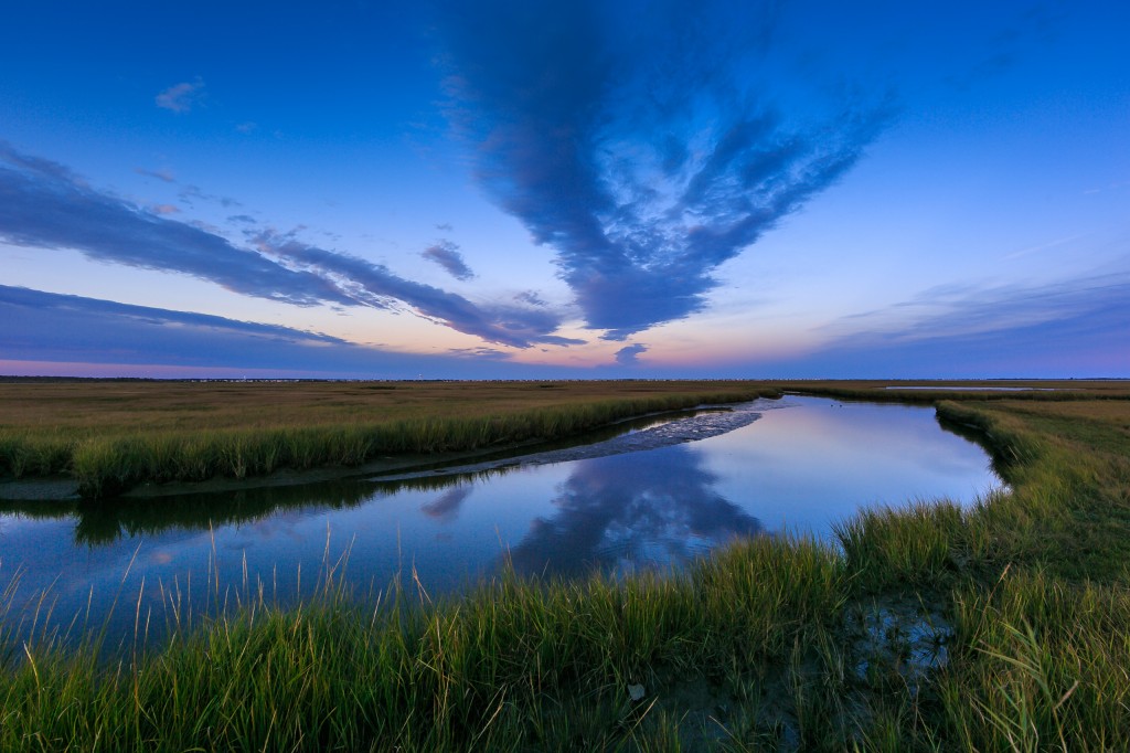 A blue hour photograph of Dock Road's north marsh on a calm Fall evening. No wind allowed a glassy reflection on the marsh estuary, mirroring the clouds