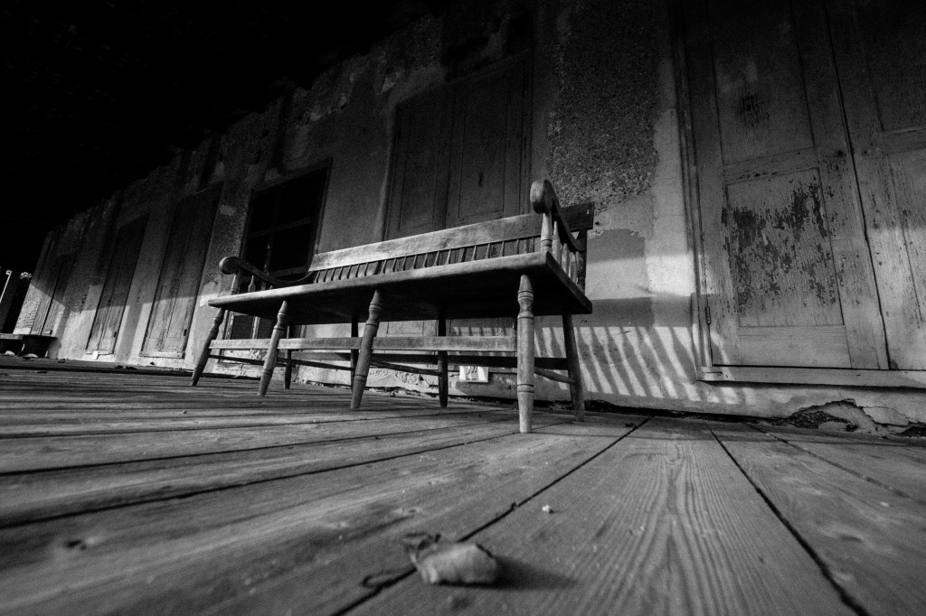 In this black and white photograph, strong leading lines move the eye through this olde tyme porch where an old wood bench sat steady for a lifetime of stories, friendship and support. 
