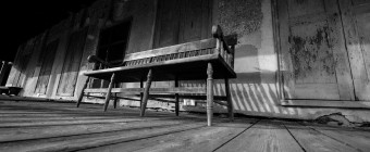 In this black and white photograph, strong leading lines move the eye through this olde tyme porch where an old wood bench sat steady for a lifetime of stories, friendship and support.