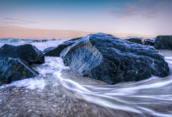 In this seascape photograph, Atlantic Ocean tidal waters ebb and flow as seawater races around jetty rock as gravity pulls the water back to the sea