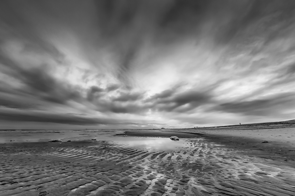 A black and white HDR photograph of fierce clouds, a tidal pool and undulating sands on the beach in Holgate, NJ. 