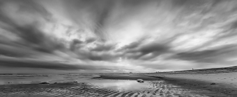 A black and white HDR photograph of fierce clouds, a tidal pool and undulating sands on the beach in Holgate, NJ.