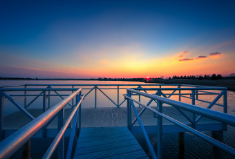 An HDR sunset photograph taken from the aluminum dock overlooking Bass River in New Gretna, New Jersey. With the metal dock marking the foreground, a rich pastel glow colors the sky and water on this near cloudless evening.