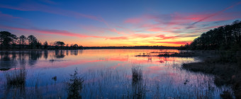 A spectacular HDR photograph taken during blue hour overlooking the front lake at the Stafford Forge Wildlife Management Area. Pastel clouds drape the horizon while marsh grasses are dormant and still in the mirrored reflection of water.