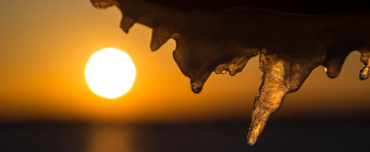 An icy handrail makes for an interesting macro shot with the setting sun over the bay off in the distance left of a sharp focused icicle.