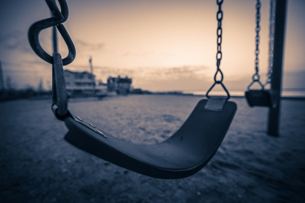 Wide angle sepia photograph of two swings over the sand at Surf City Sunset Park