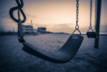 Wide angle sepia photograph of two swings over the sand at Surf City Sunset Park
