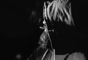 Ceramicist and potter, a hooded Jeff Ruemeli smokes the last of his cigarette as he stokes the soda kiln fires in this low key black and white portrait.