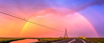 Photograph of a double rainbow arching over power lines and Dock Road at sunset