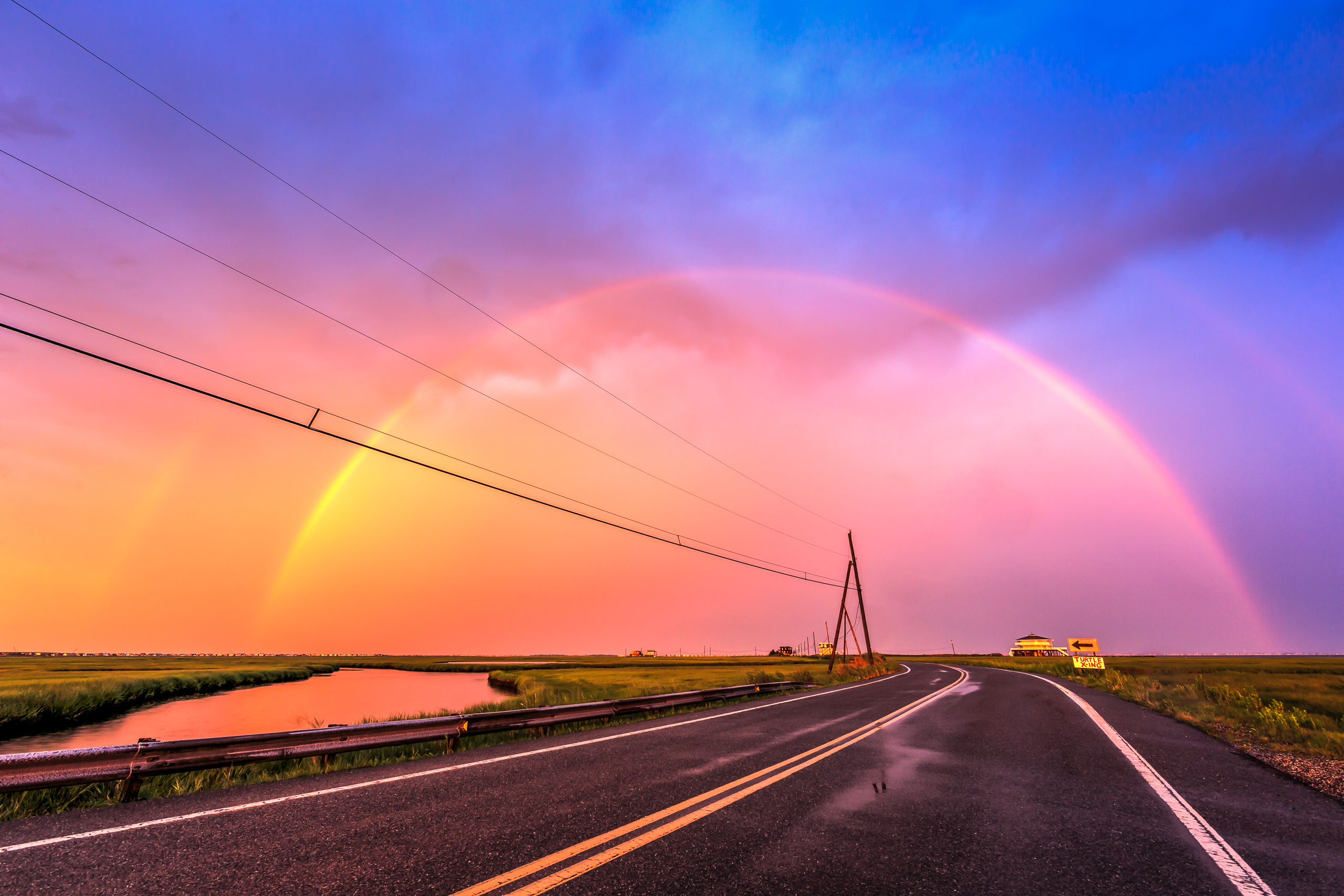 Photograph of a double rainbow arching over power lines and Dock Road at sunset