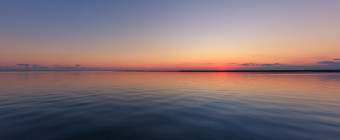 Wide angle landscape photograph of calm bay water and clear sky at blue hour