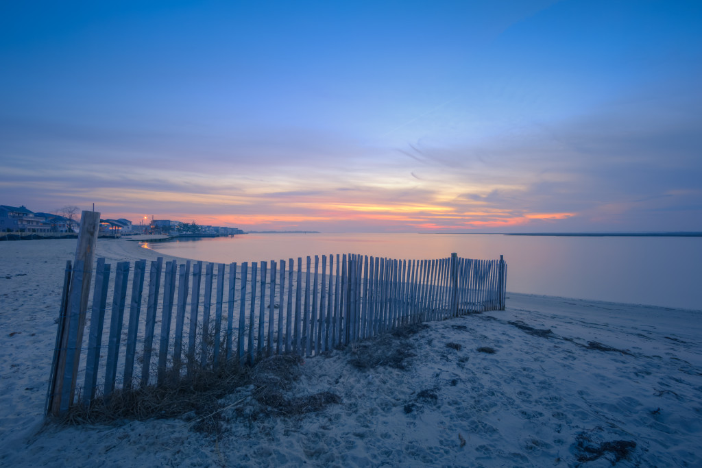 Blue hour HDR photograph overlooking dune fence and calm bay water