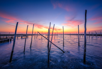 Sunset photograph of frozen bay ice locking in marina posts