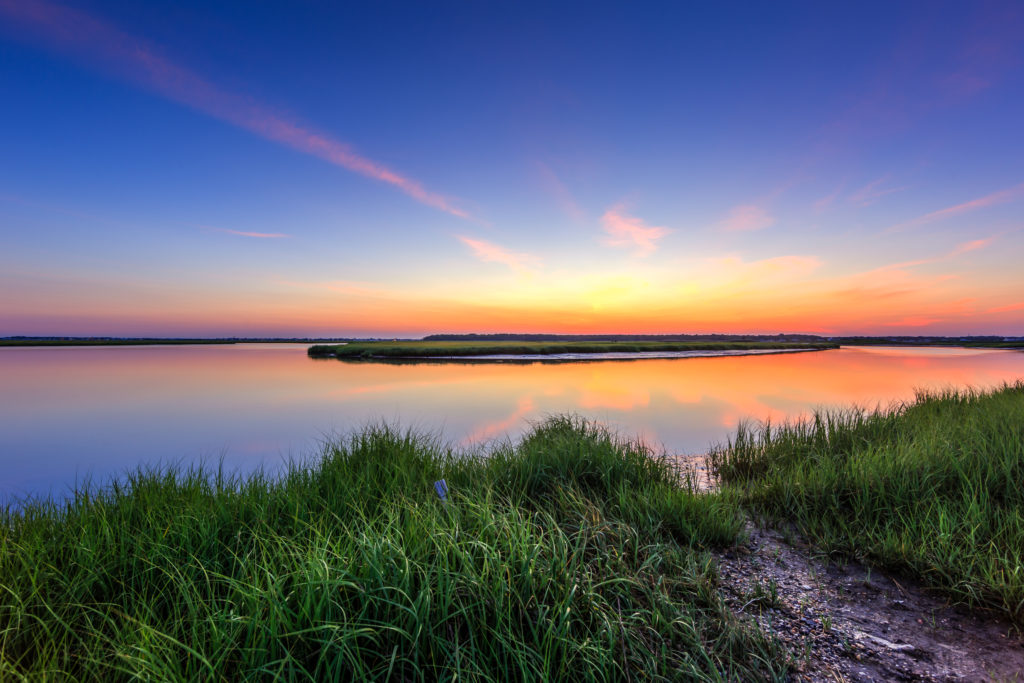 Sunset photograph of dead calm conditions highlighting vibrant green marsh grass just after sunset.