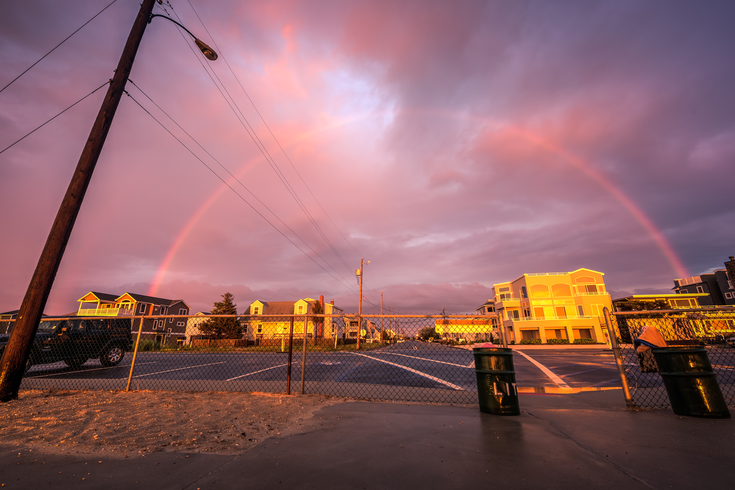 Wide angle HDR photograph of a rainbow forming over Long Beach Island houses bathed in gold.