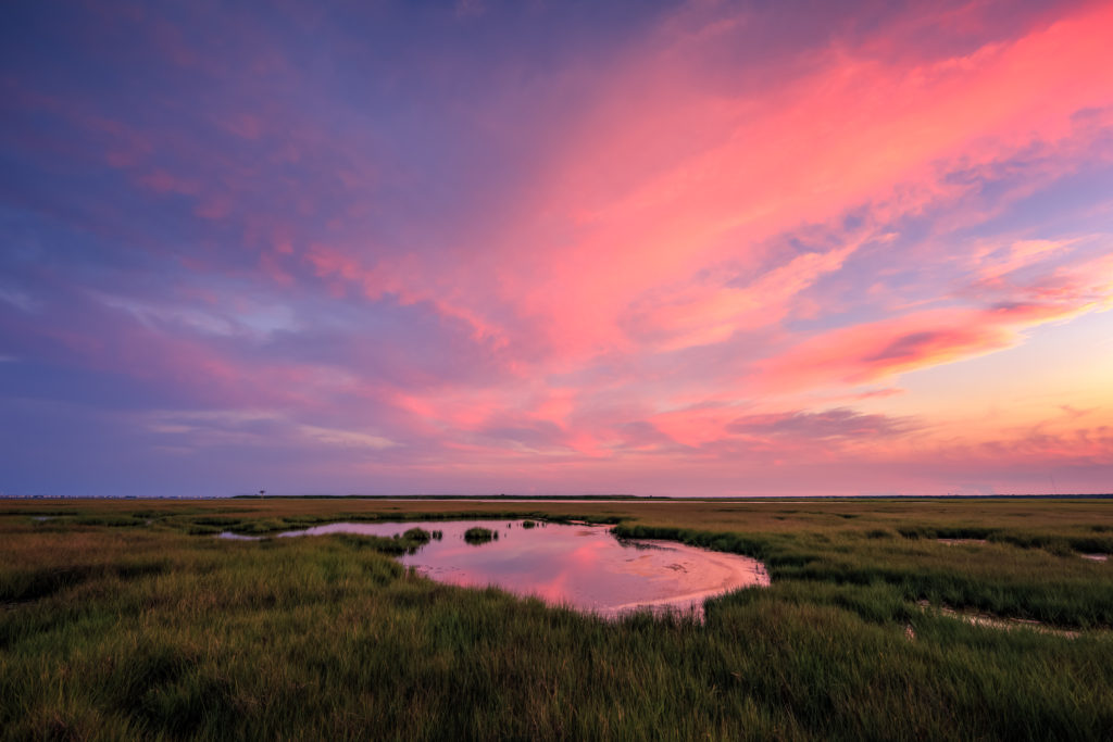 Landscape photograph of a pastel sunset sky over a summer salt marsh.