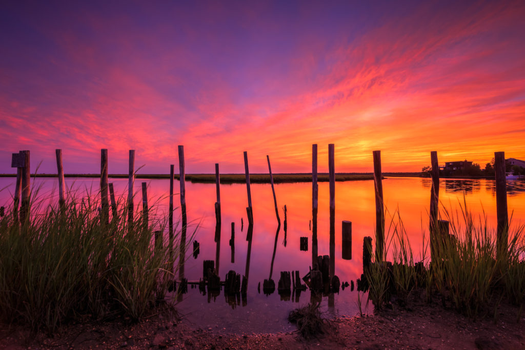 Fiery sunset ignites with stunning marsh tributary reflection.