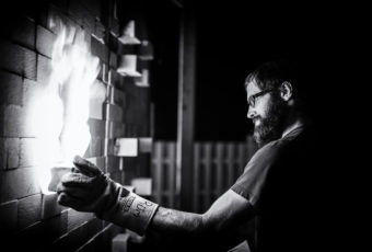Black and white photograph of Jeff Ruemeli working a soda kiln.