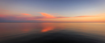Motion blur sunset photo of pastel clouds and calm bay water.