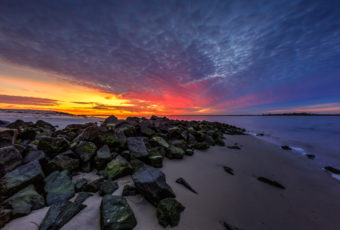 Bayside sunset photo over sand and jetty rock.
