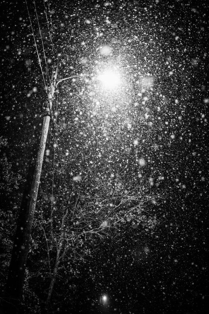 Low key black and white photo of heavy snow lit by streetlight.