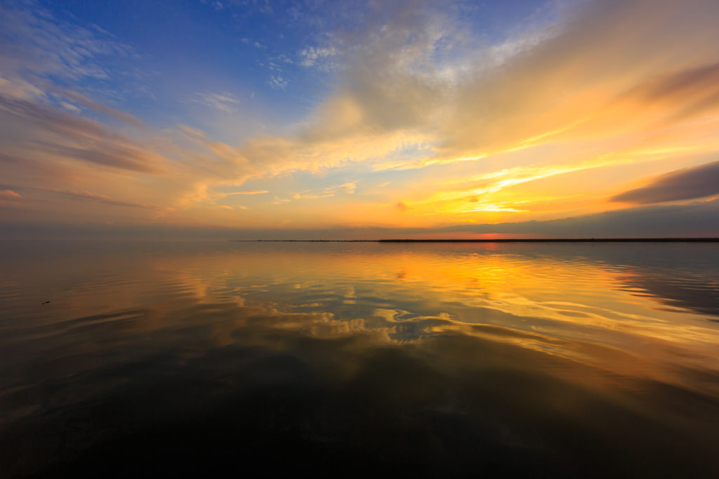 Golden hour photo lights the sky over calm bay water.