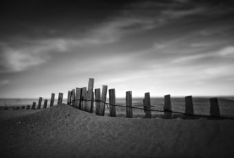 Strong contrast black and white photo of sand dune enveloping sand fence.