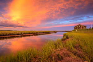 Explosive sunset photo over salt marsh, water, and house.