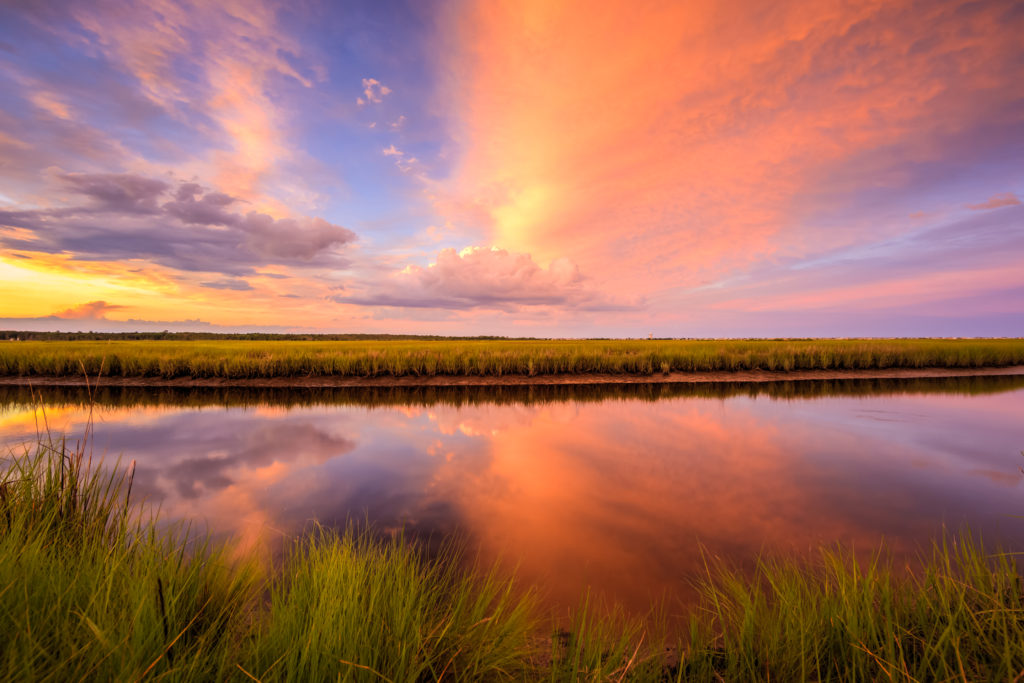 Sunset photo ignites over marsh and reflective water.