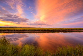 Sunset photo ignites over marsh and reflective water.