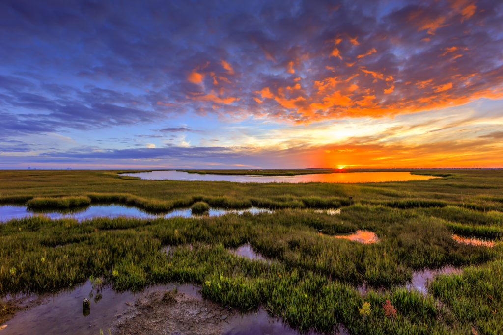 Photo of a fiery sunset over marsh and tidal pools.