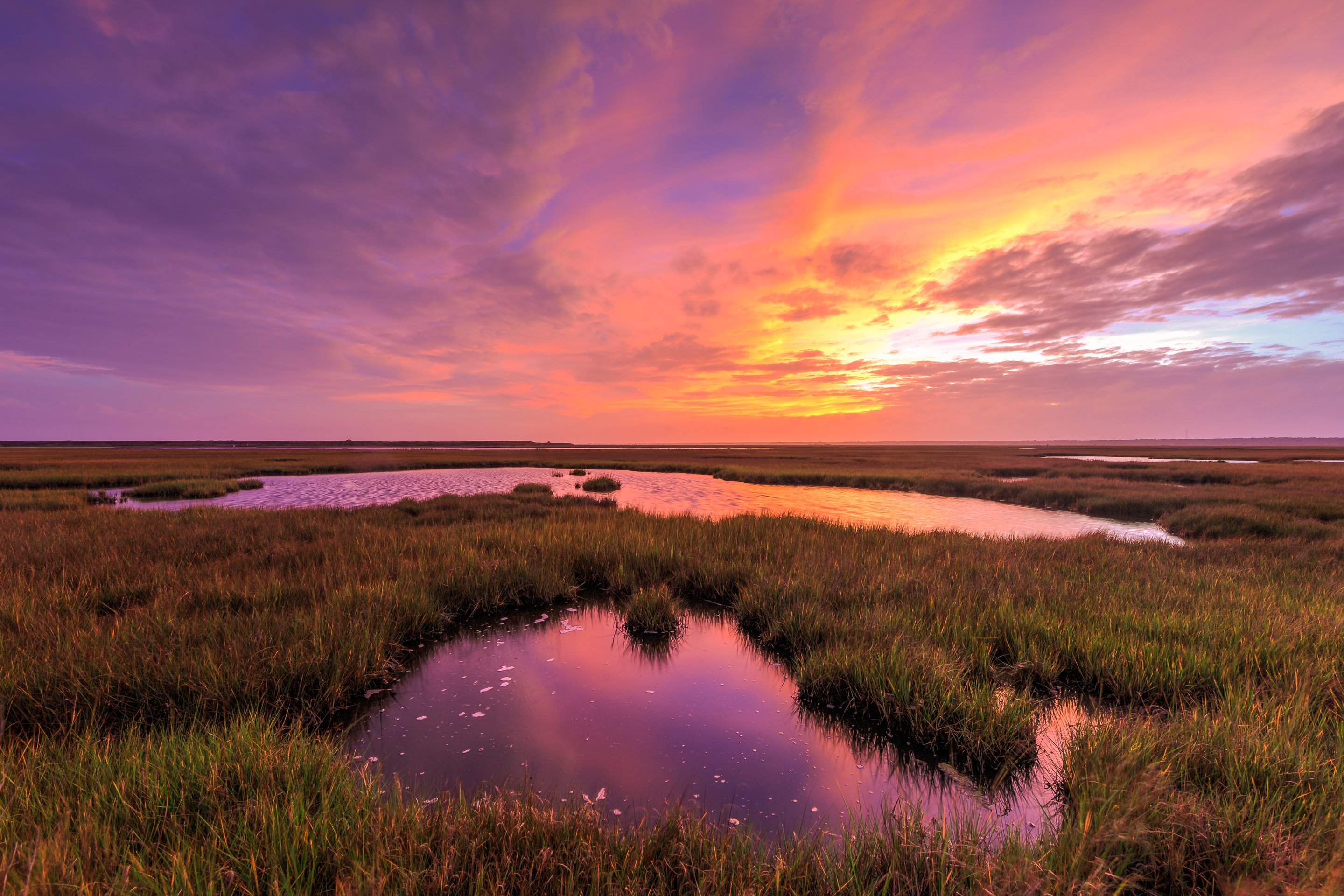 Pink and purple sunset photo over salt marsh.