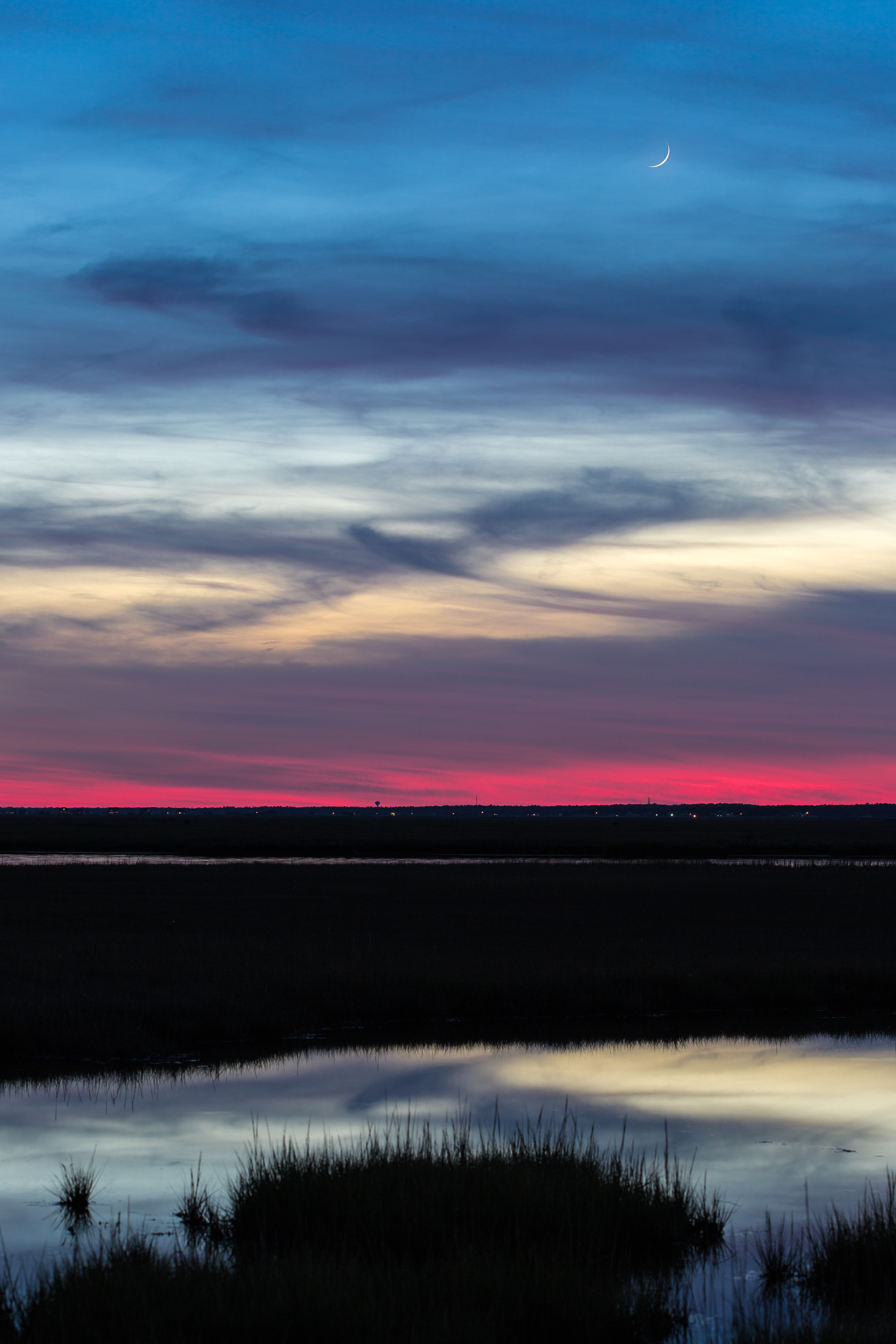 Crescent moonrise over salt marsh at blue hour.