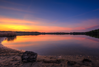 Sunset photo over sand and a calm pond.