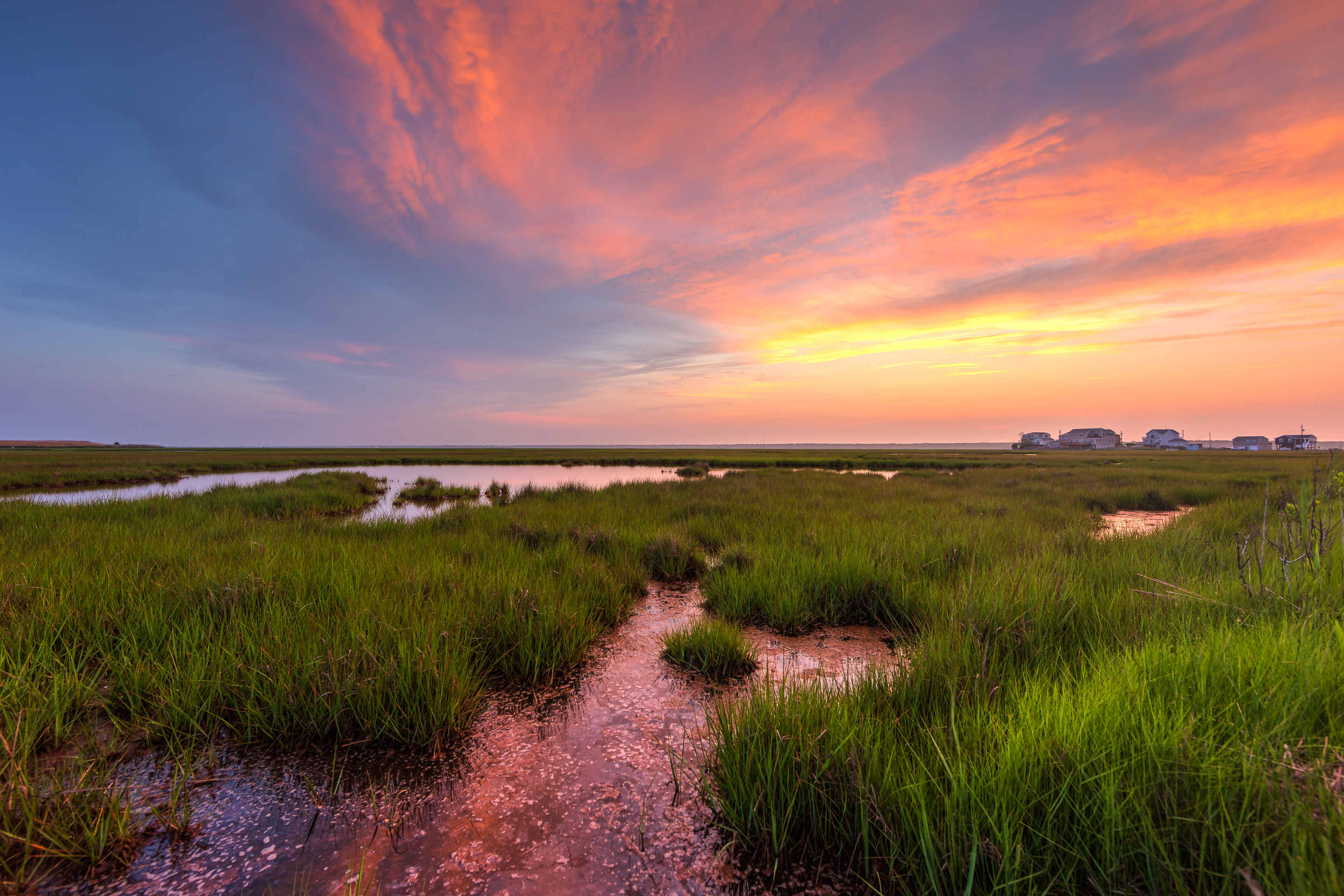 Sunset photo of pastel color clouds over reflective water and green salt marsh.