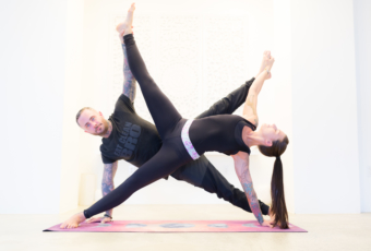 Yogis Rose Dease and Jesse Holt form an 'X' in a partner yoga pose.