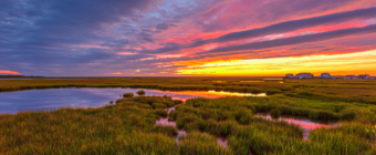 14mm wide angle HDR sunset photo made over late summer salt marsh with a five distant homes in the background.