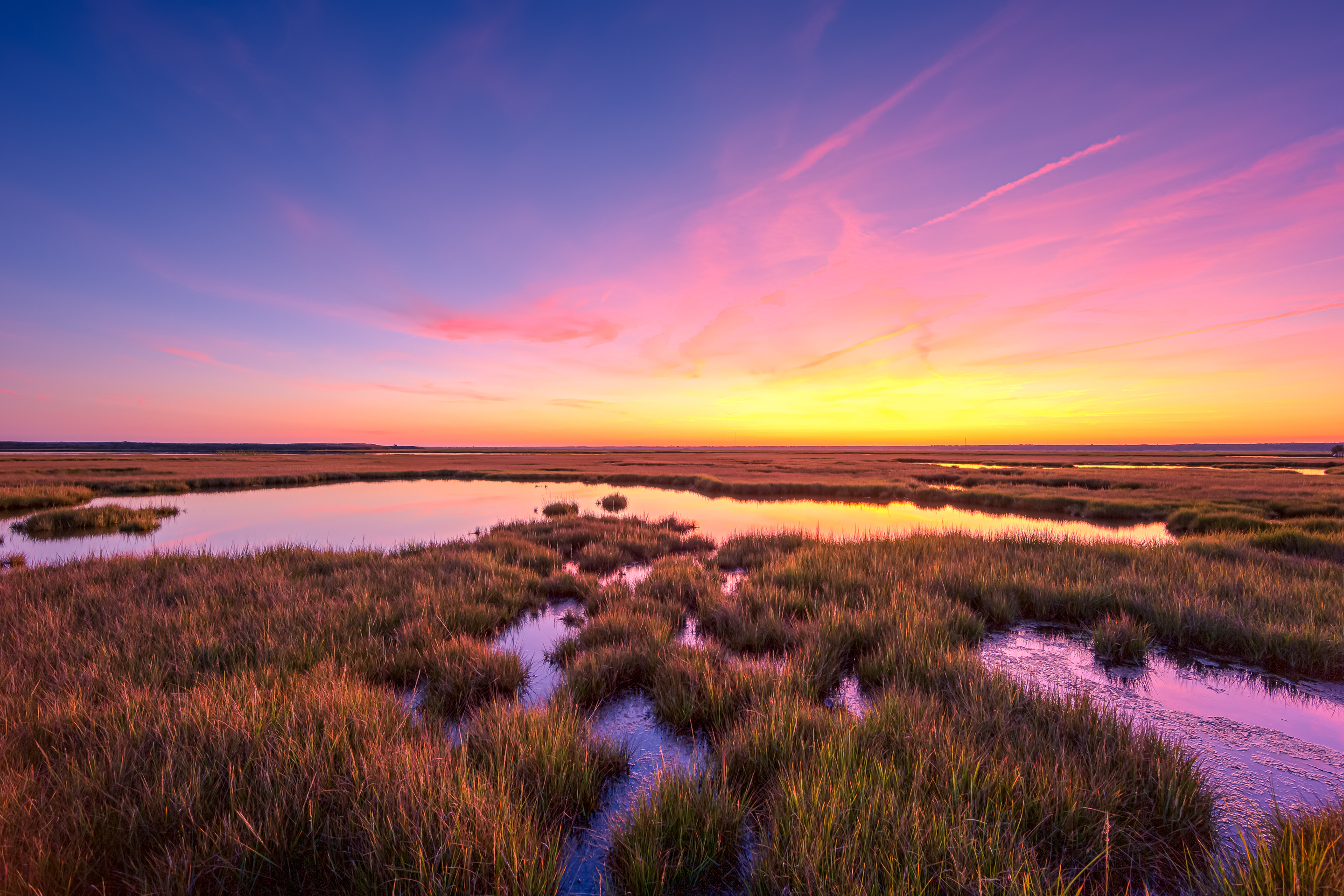 14mm wide angle sunset photo with pastel colored clouds over a still salt marsh.