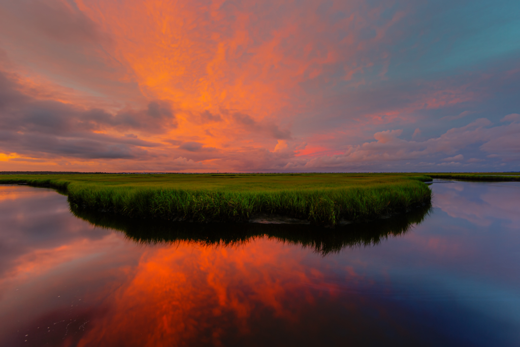 14mm wide angle sunset photo with intense pastel colored mammatus clouds smoldering over Cedar Rund Dock Road's salt marsh and still, reflective water.