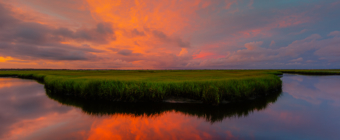 14mm wide angle sunset photo with intense pastel colored mammatus clouds smoldering over Cedar Rund Dock Road's salt marsh and still, reflective water.